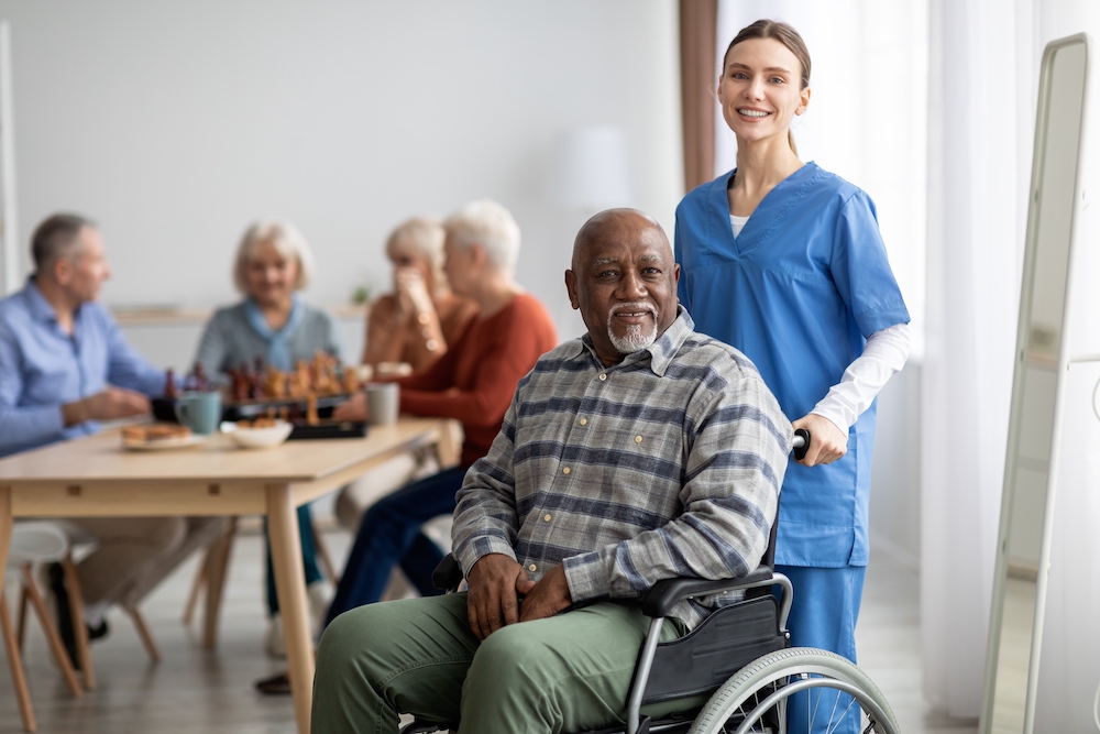A senior man in a wheelchair with a happy female caregiver in a community room
