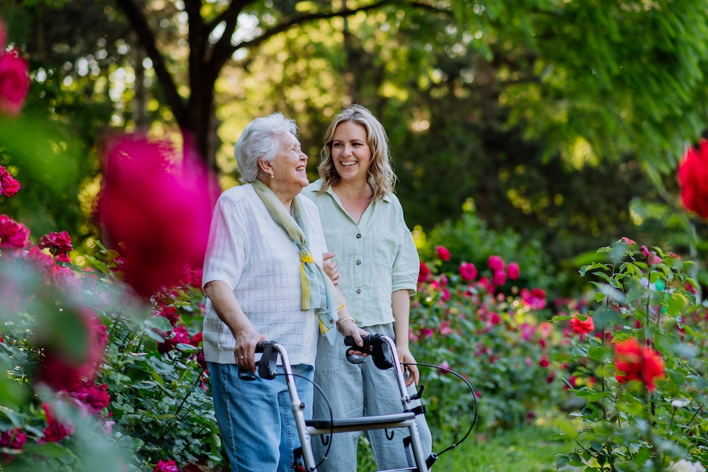 A senior woman and her daughter talk while walking around the grounds at one of the memory care facilities in Vista